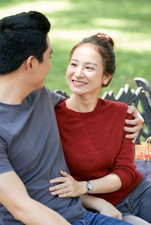 Pretty young Asian woman smiling and looking at her boyfriend when they are resting on bench